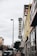 A street view featuring a vintage vertical sign that reads 'Johnson Storage Moving' on the side of a building. The surrounding area includes various storefronts, parked cars along the sidewalk, and a speed limit sign indicating 30 mph. A painted teddy bear mural can be seen near the top of one building, and the sky is overcast, adding a muted tone to the scene.