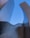 Tall, curved architectural structures made of metallic materials reach towards a clear blue sky. The surfaces reflect light, creating a sleek and modern appearance.