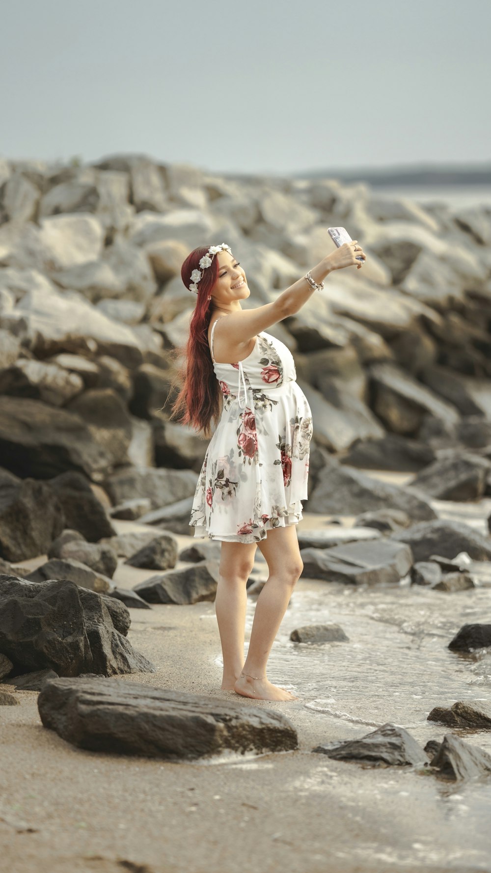 mulher no vestido floral branco vermelho e azul que está de pé na areia cinzenta durante o dia