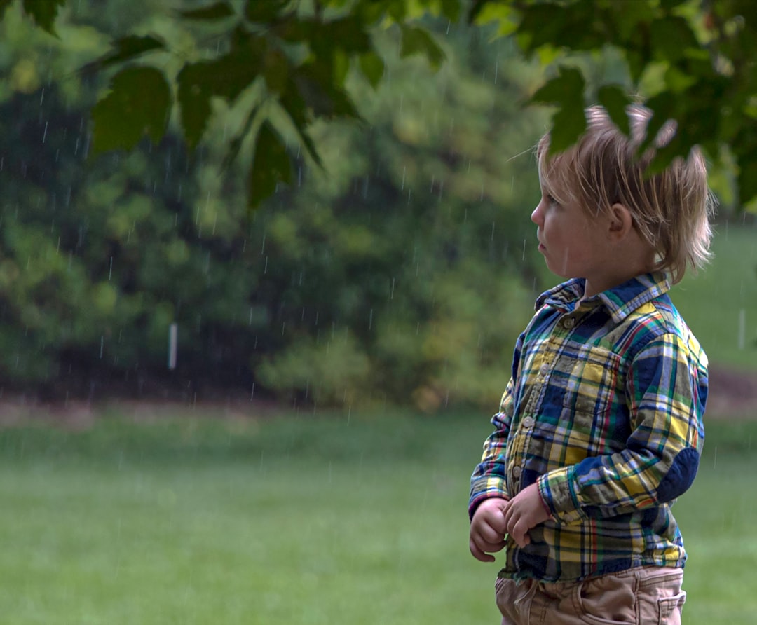 boy in blue white and red plaid dress shirt standing on green grass field during daytime