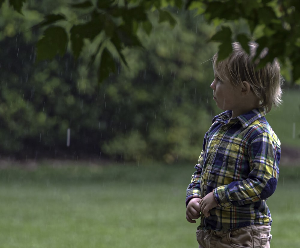 boy in blue white and red plaid dress shirt standing on green grass field during daytime