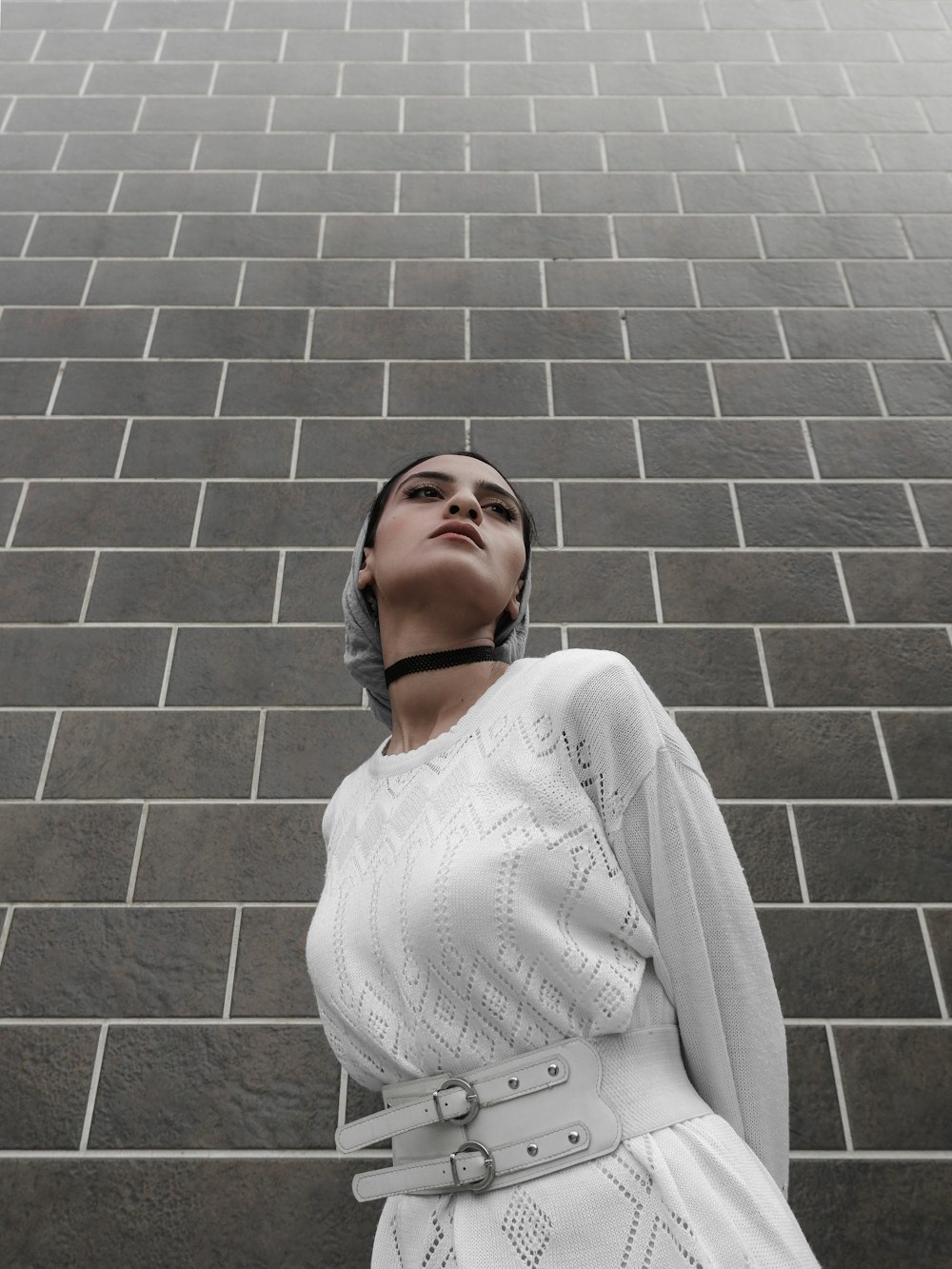 woman in white sweater standing beside brick wall