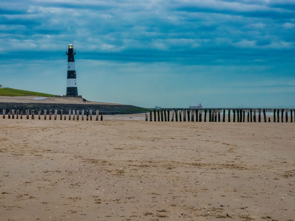black and white lighthouse on brown sand under blue sky during daytime