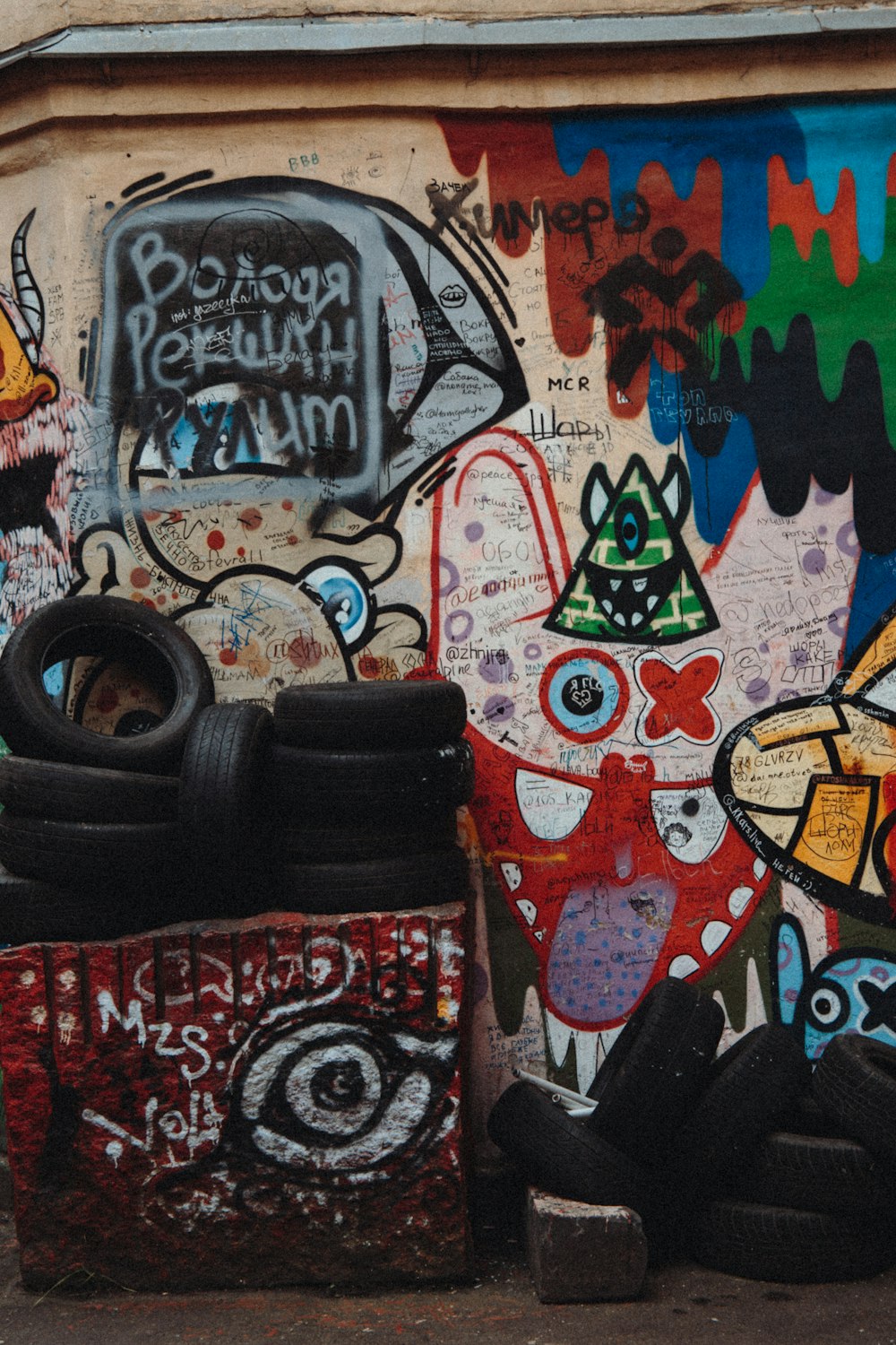 a wall covered in lots of graffiti next to a trash can