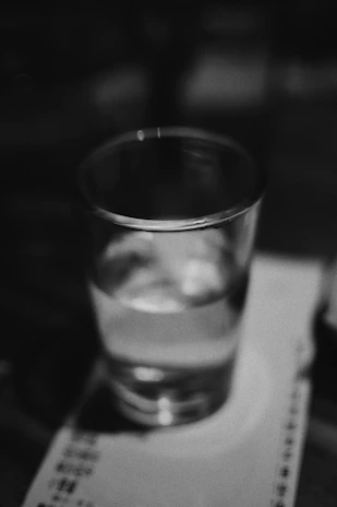 A clean, clear glass of water with a blurred water filter system in the background.