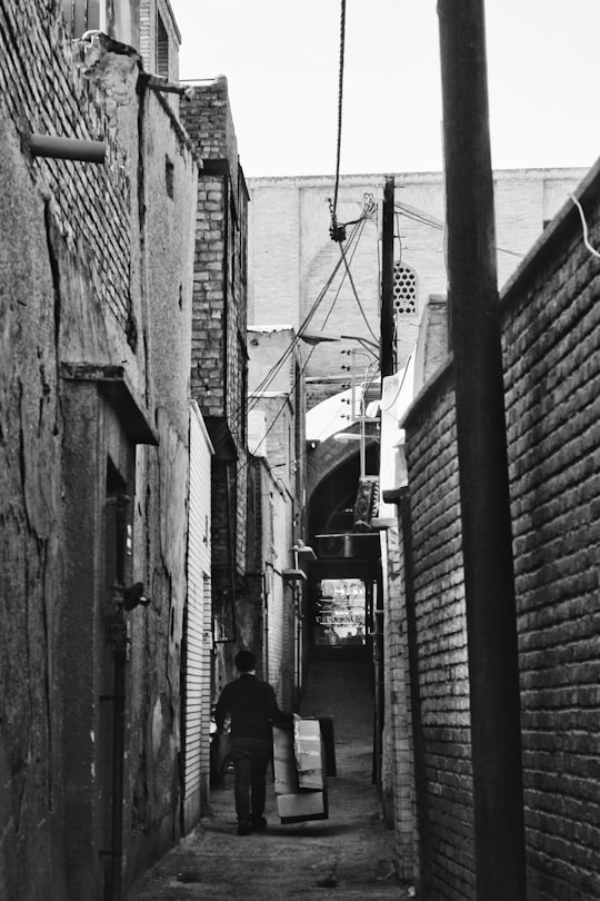 grayscale photo of a man in black jacket walking on the street in Isfahan Province Iran