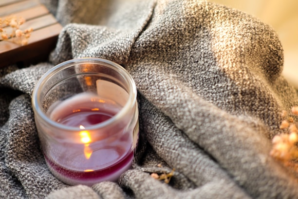 Close-up of a handcrafted candle glowing softly on a beige linen cloth with dried flowers around.