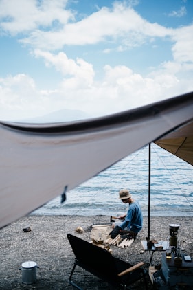 man in blue jacket sitting on white chair looking at the sea during daytime