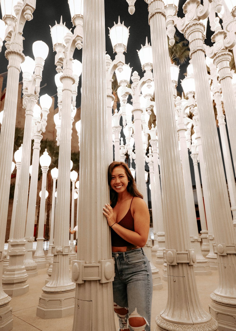woman in black tank top and blue denim jeans standing near white concrete pillars during daytime