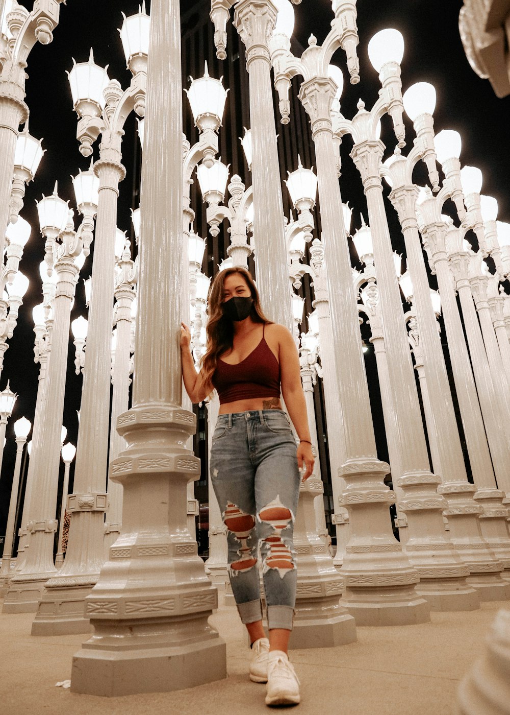 woman in orange tank top and blue denim shorts standing on white concrete pillars during daytime