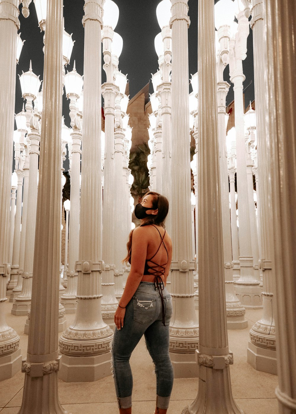 man in orange shirt and blue denim jeans standing in front of white concrete pillar during