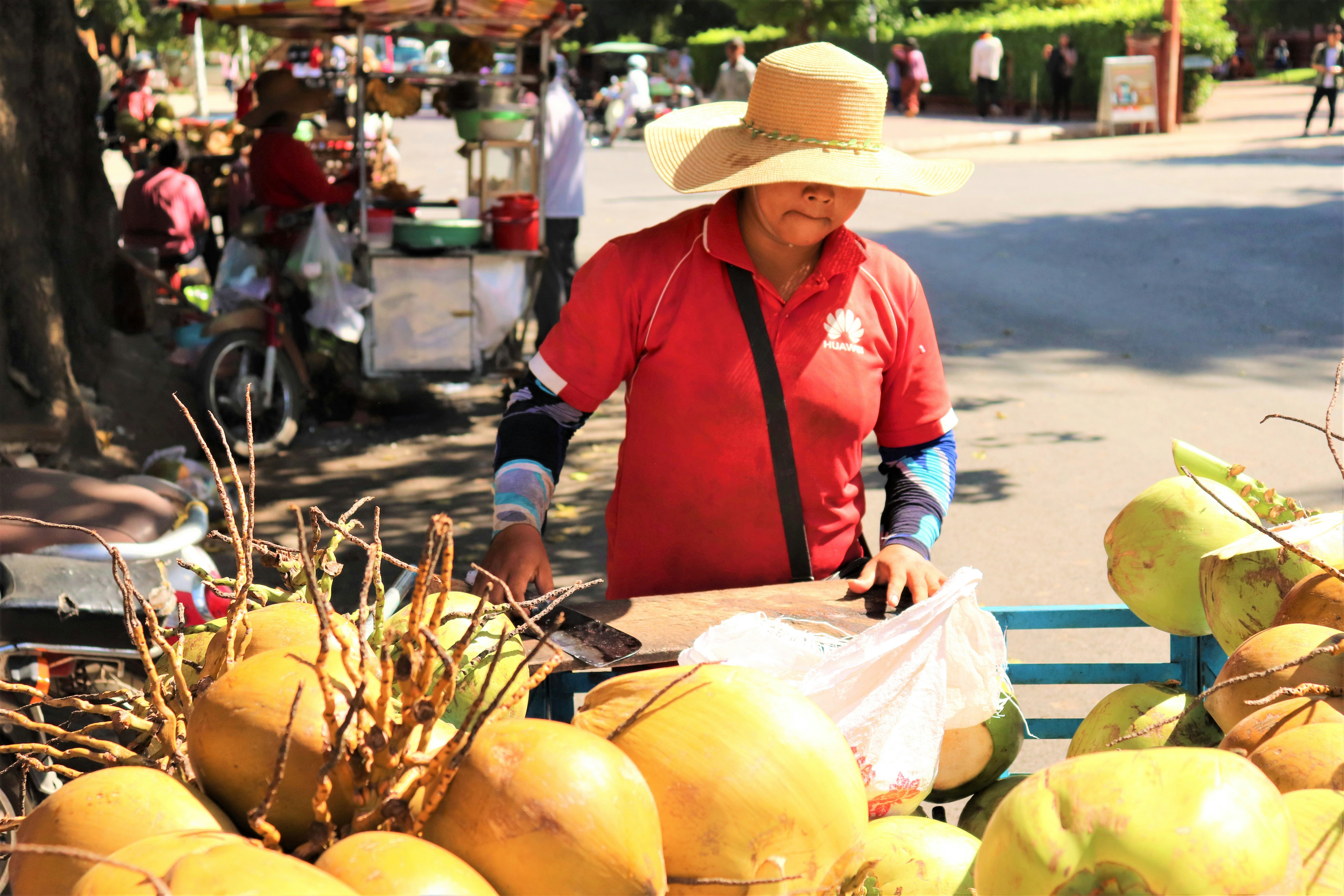 mulher na camisa de manga comprida vermelha e preta e chapéu de sol bege segurando frutas amarelas