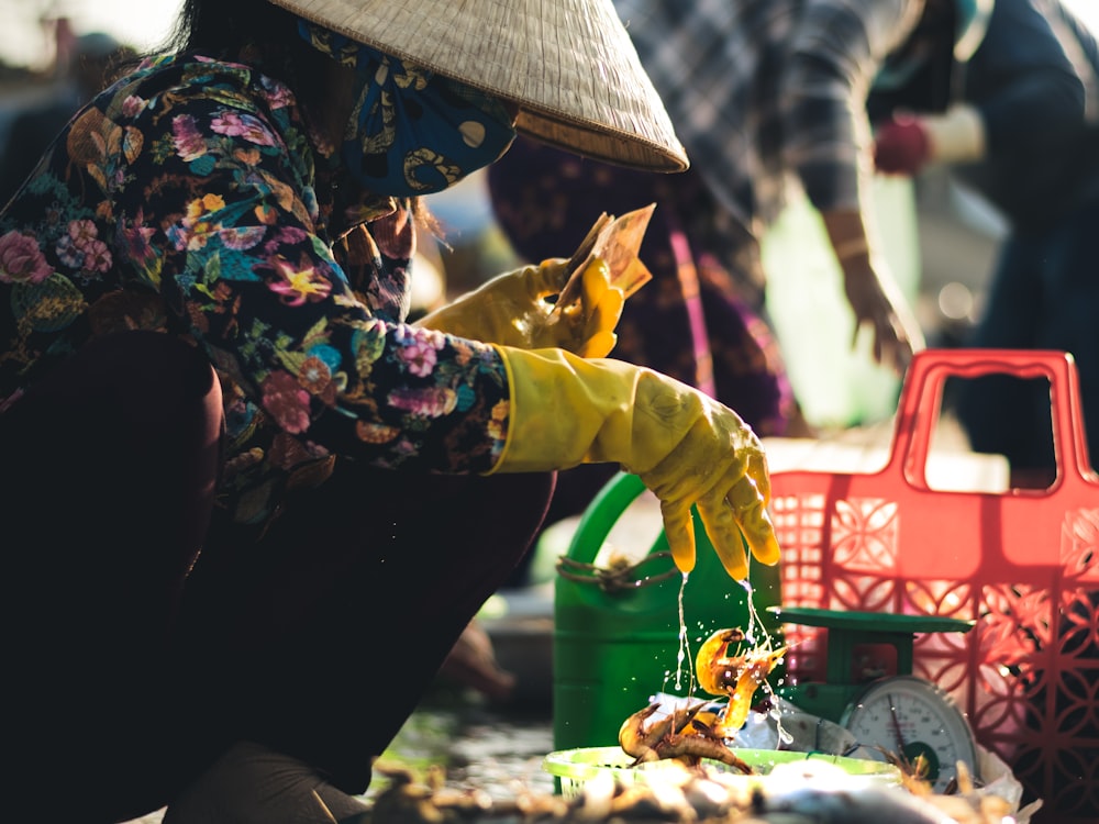 woman in green and black floral long sleeve shirt and black pants holding red plastic crate