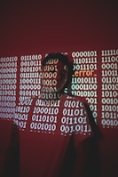 A person stands against a red background with binary code projected across their face and body. The word 'error' is prominently displayed in the projection.