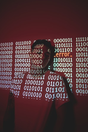 A person stands against a red background with binary code projected across their face and body. The word 'error' is prominently displayed in the projection.