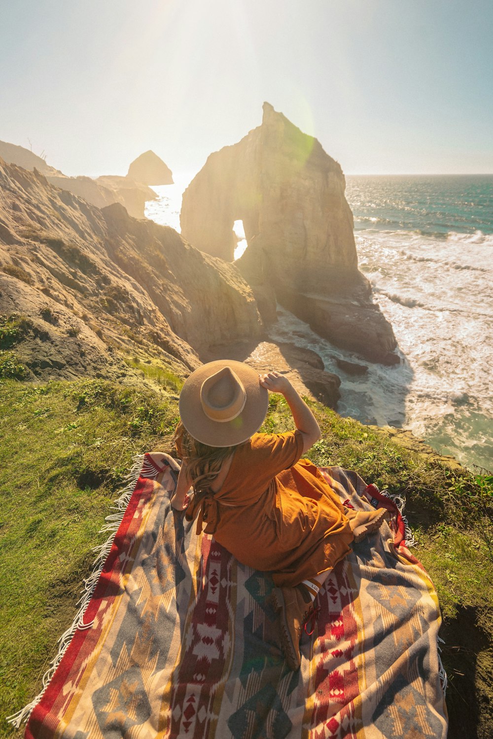 낮 동안 바위 형성에 앉아 갈색 태양 모자를 쓰고 갈색과 흰색 드레스를 입은 여자