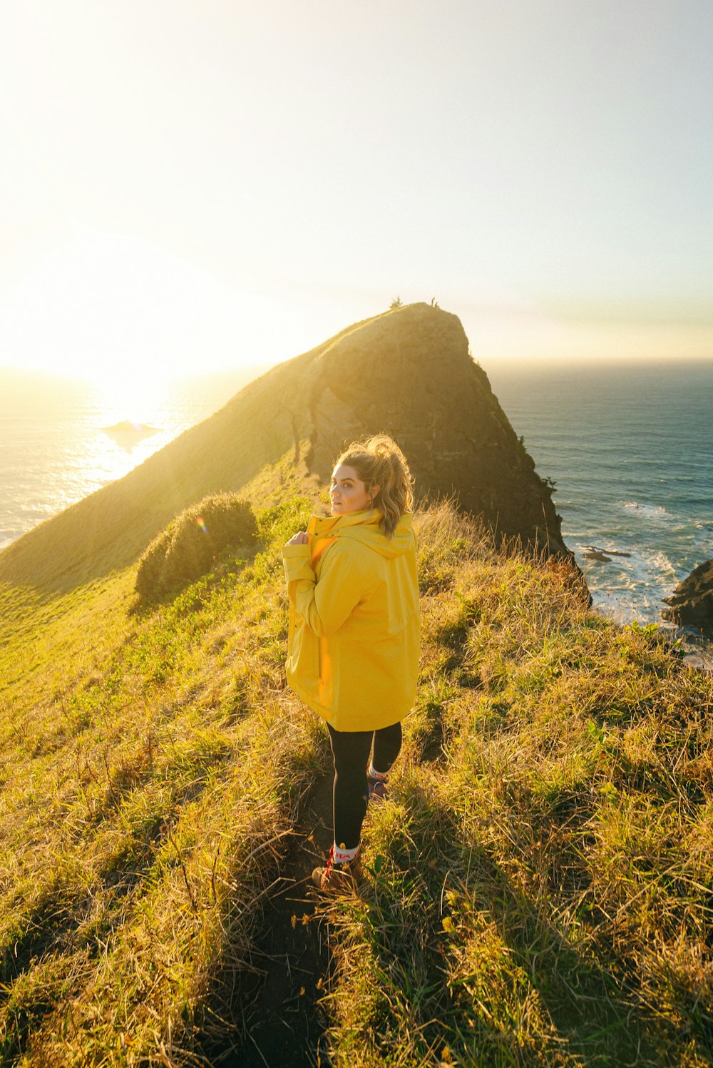 woman in yellow jacket standing on green grass field near body of water during daytime