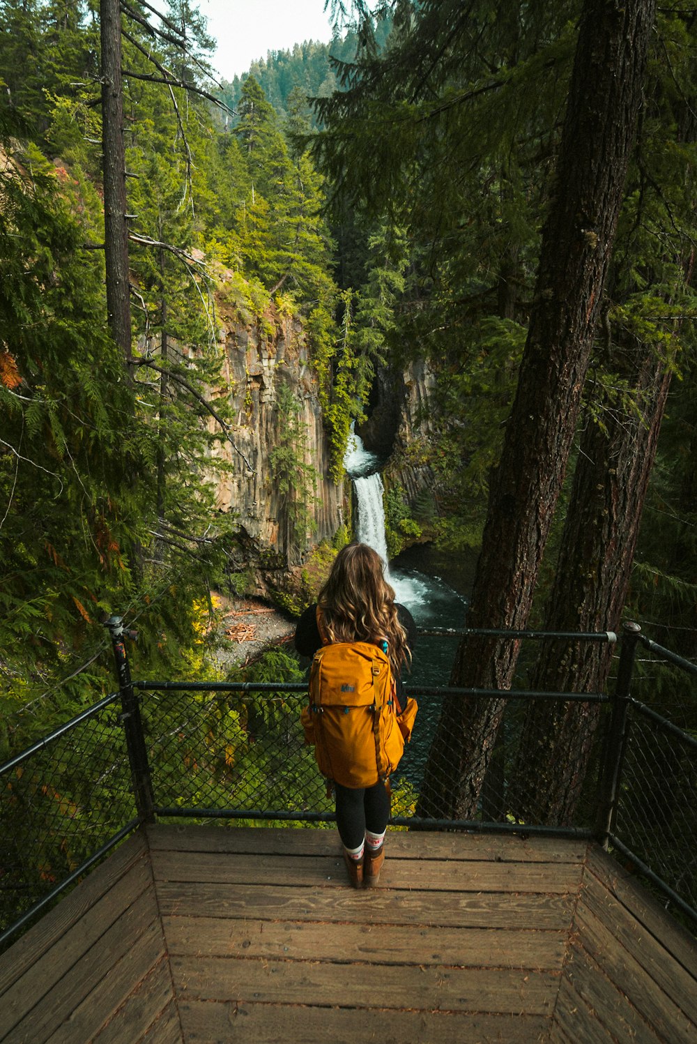 Frau in gelber Jacke steht auf Hängebrücke