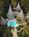 A resort-style setting with several cone-shaped thatched-roof huts surrounded by lush tropical vegetation. A vibrant blue swimming pool is centrally located on a wooden deck, with pathways winding through neatly manicured gardens.