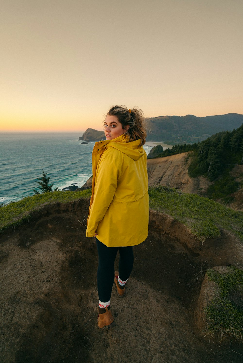 woman in yellow coat standing on brown dirt road near body of water during daytime