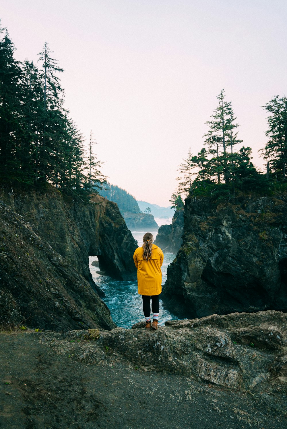 man in yellow jacket and blue denim jeans standing on rocky hill during daytime