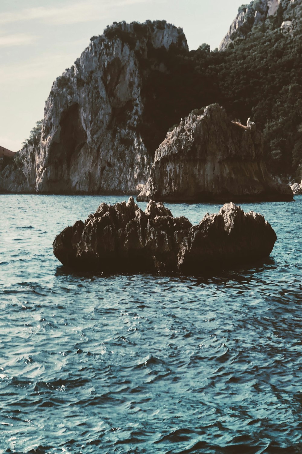 person in black shorts standing on rock formation in the middle of sea during daytime