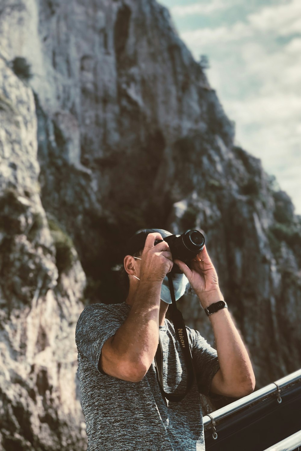 man in grey shirt taking photo of grey rock formation during daytime