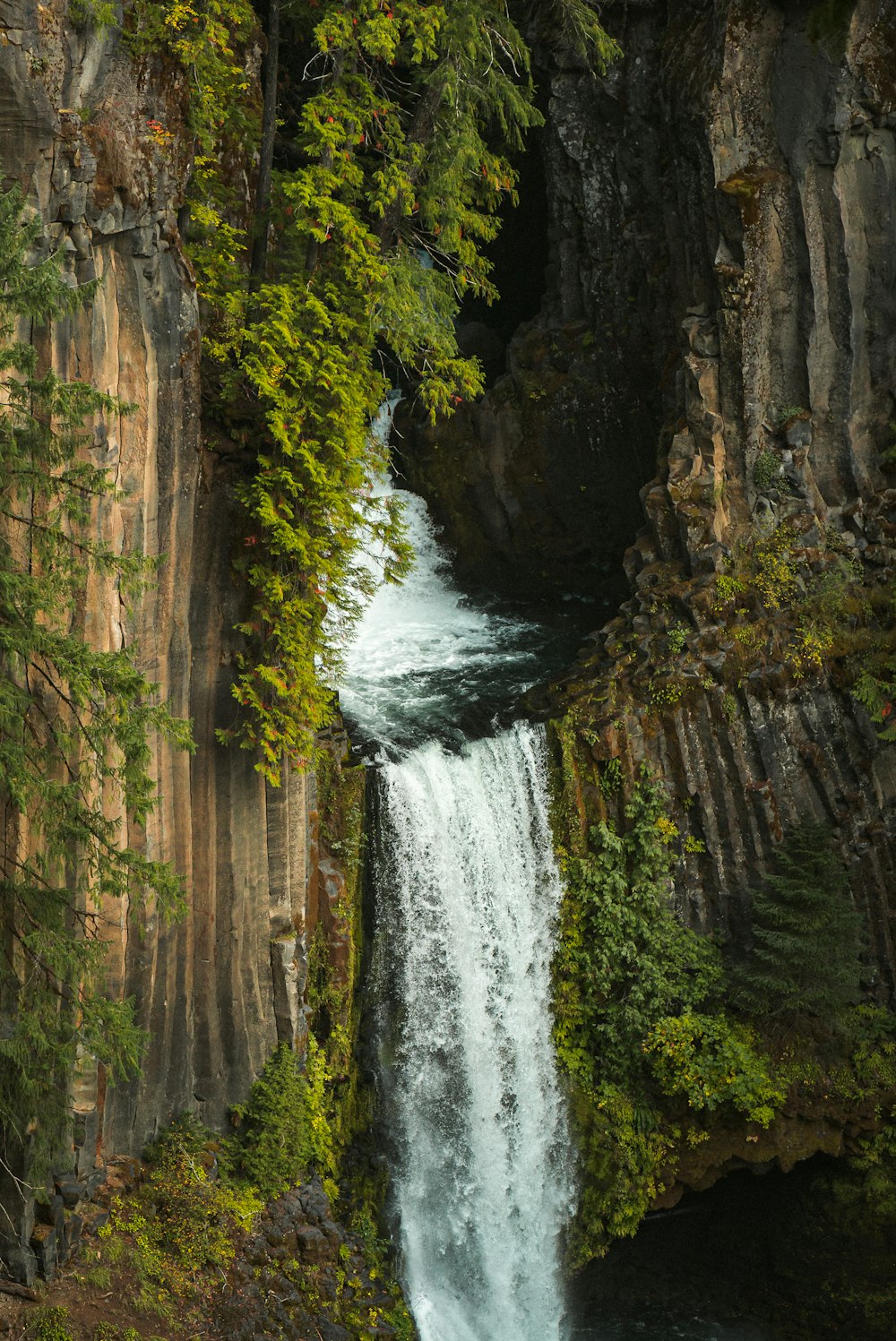 water falls between brown and green rock formation during daytime