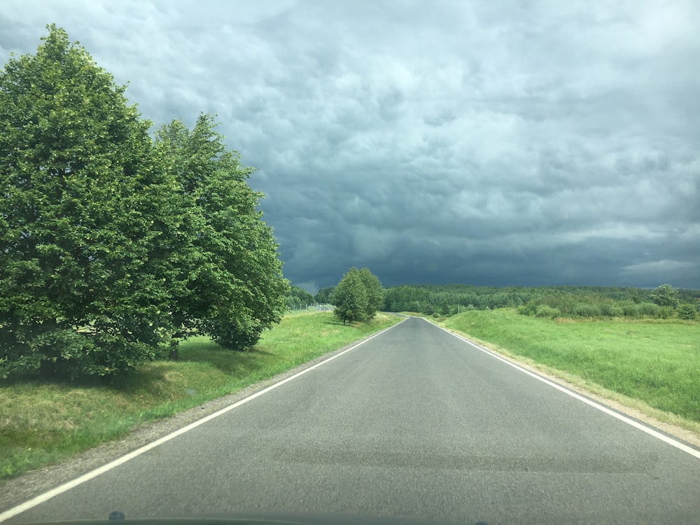 昼間の白い雲の下の緑の木々の間の灰色のアスファルト道路