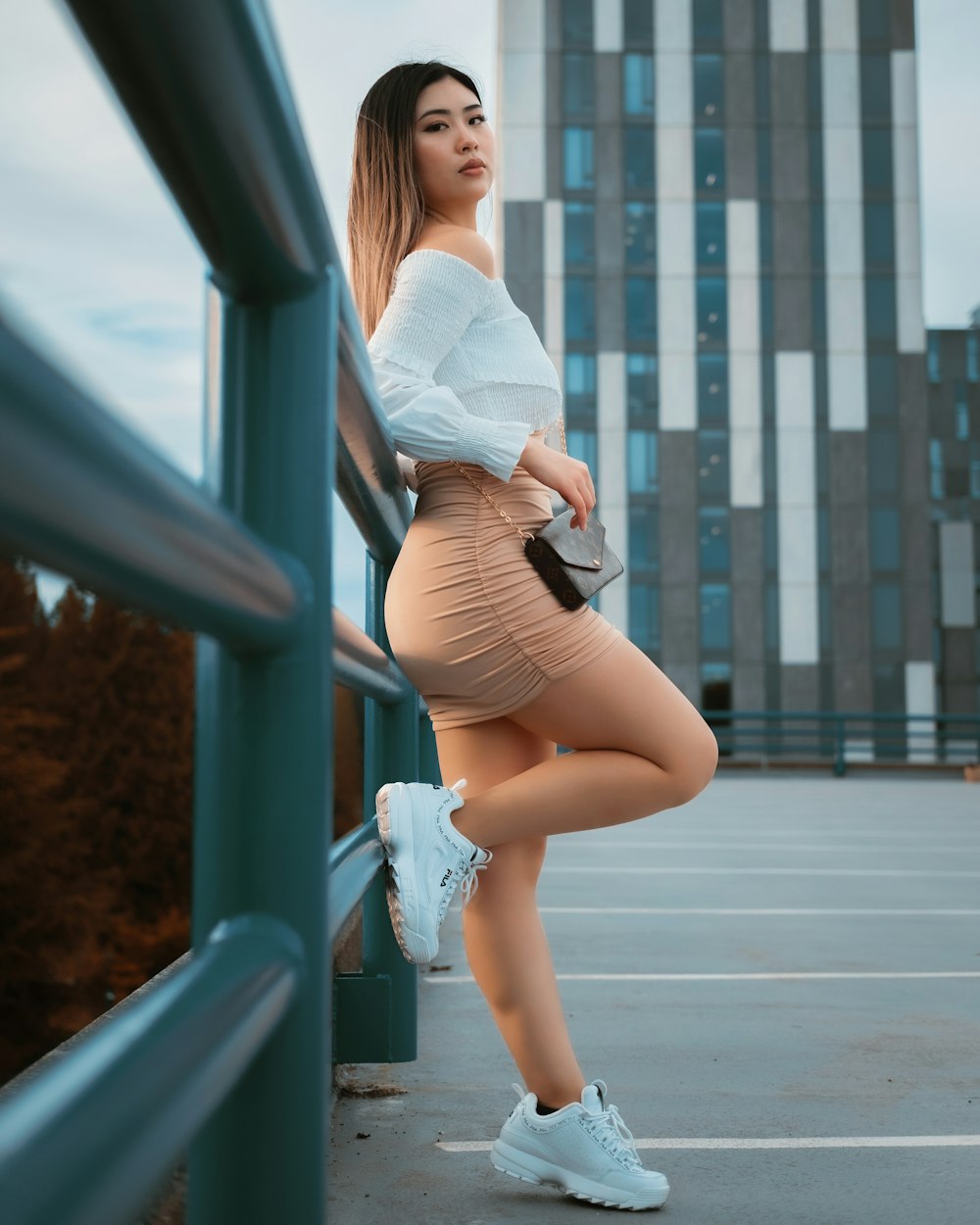 woman in white shirt and brown skirt leaning on blue metal railings