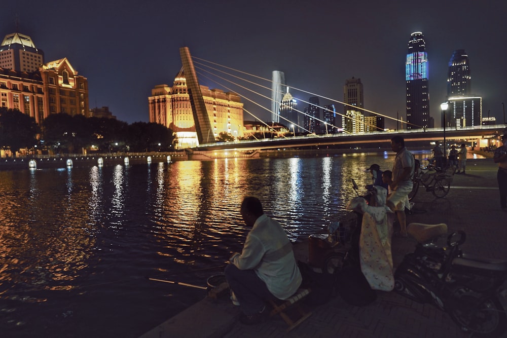 man in white long sleeve shirt sitting on brown wooden dock during night time