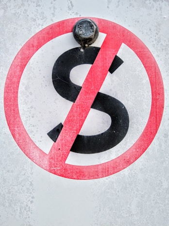 A sign displays a black letter 'S' with a red circle and diagonal line across it, indicating a prohibition. The background has a textured, weathered appearance, and a metal bolt is situated at the top of the sign.