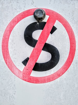 A sign displays a black letter 'S' with a red circle and diagonal line across it, indicating a prohibition. The background has a textured, weathered appearance, and a metal bolt is situated at the top of the sign.
