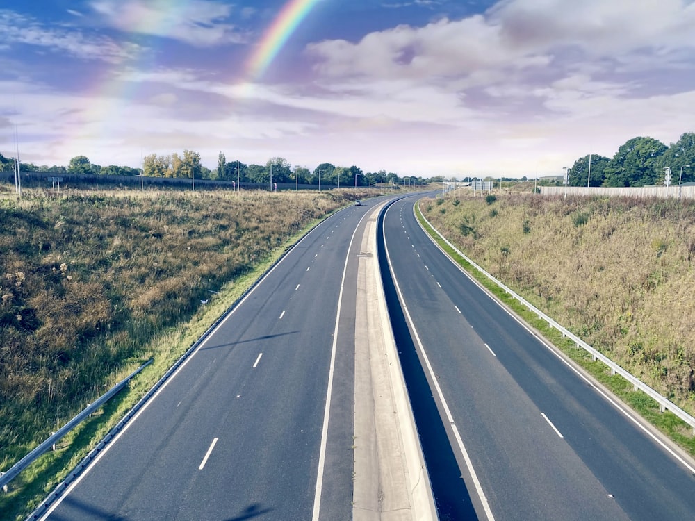 gray concrete road between green grass field under blue sky and white clouds during daytime