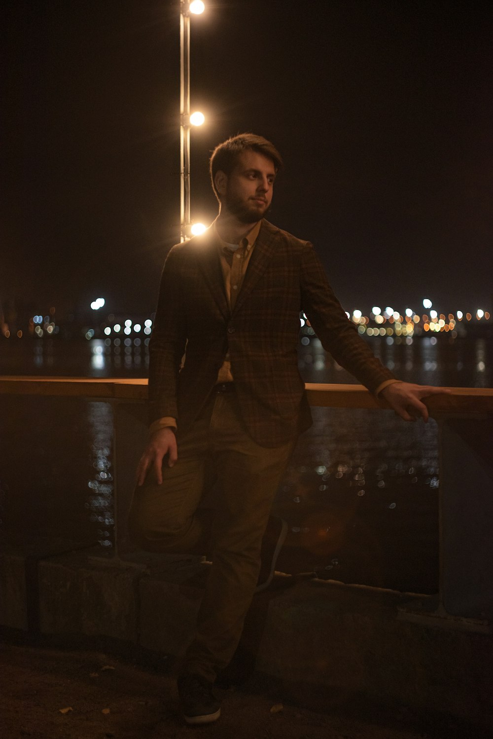 man in black suit jacket and brown pants standing beside brown wooden table