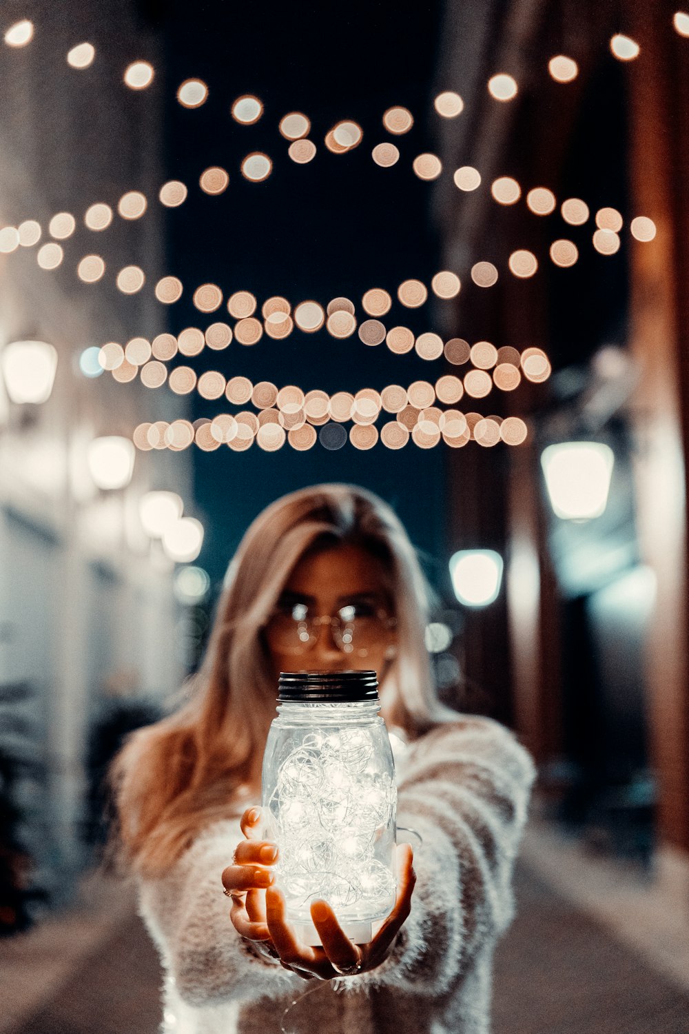 透明なガラス瓶を持つ白いセーターの女性