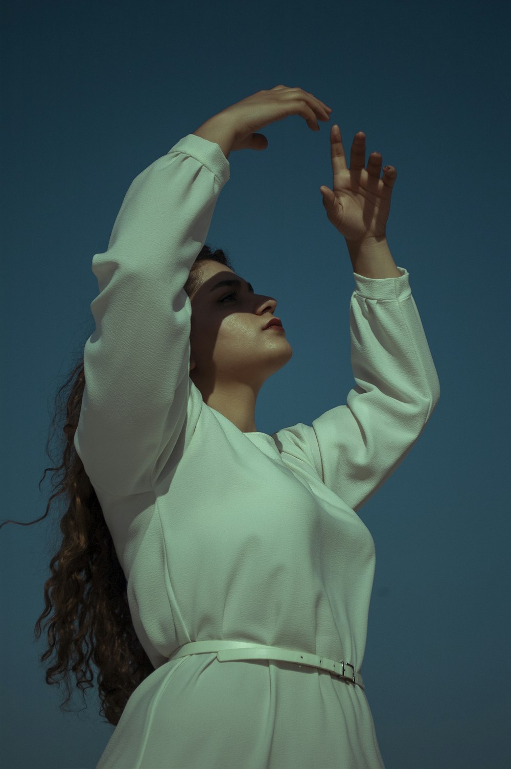 woman in white long sleeve shirt covering her face with her hands