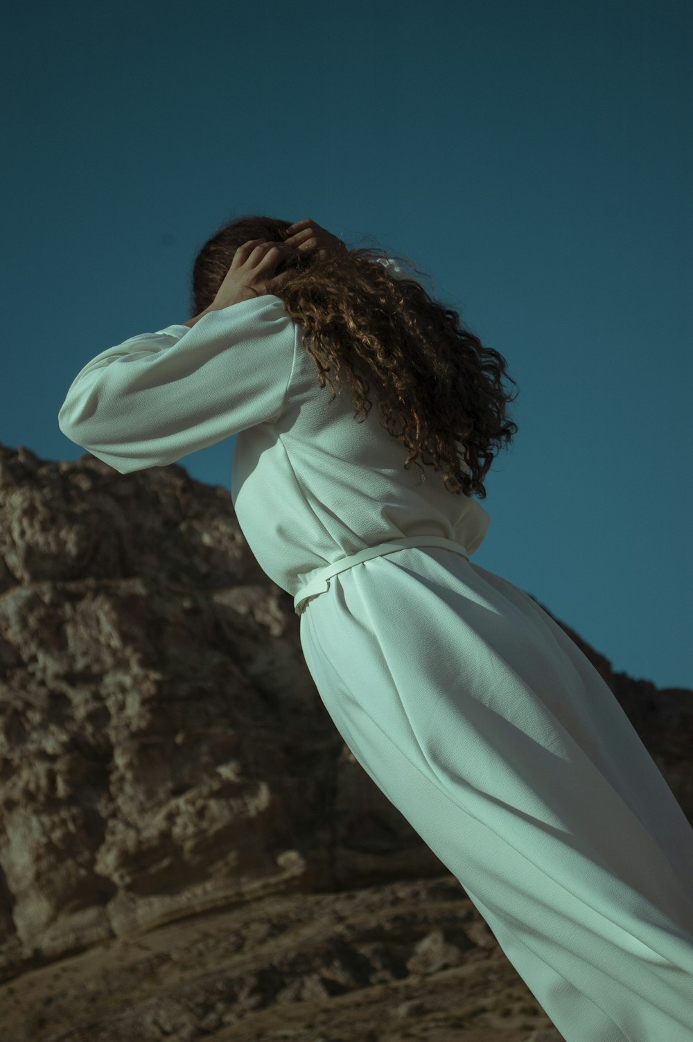 woman in white hoodie standing on brown rock formation during daytime