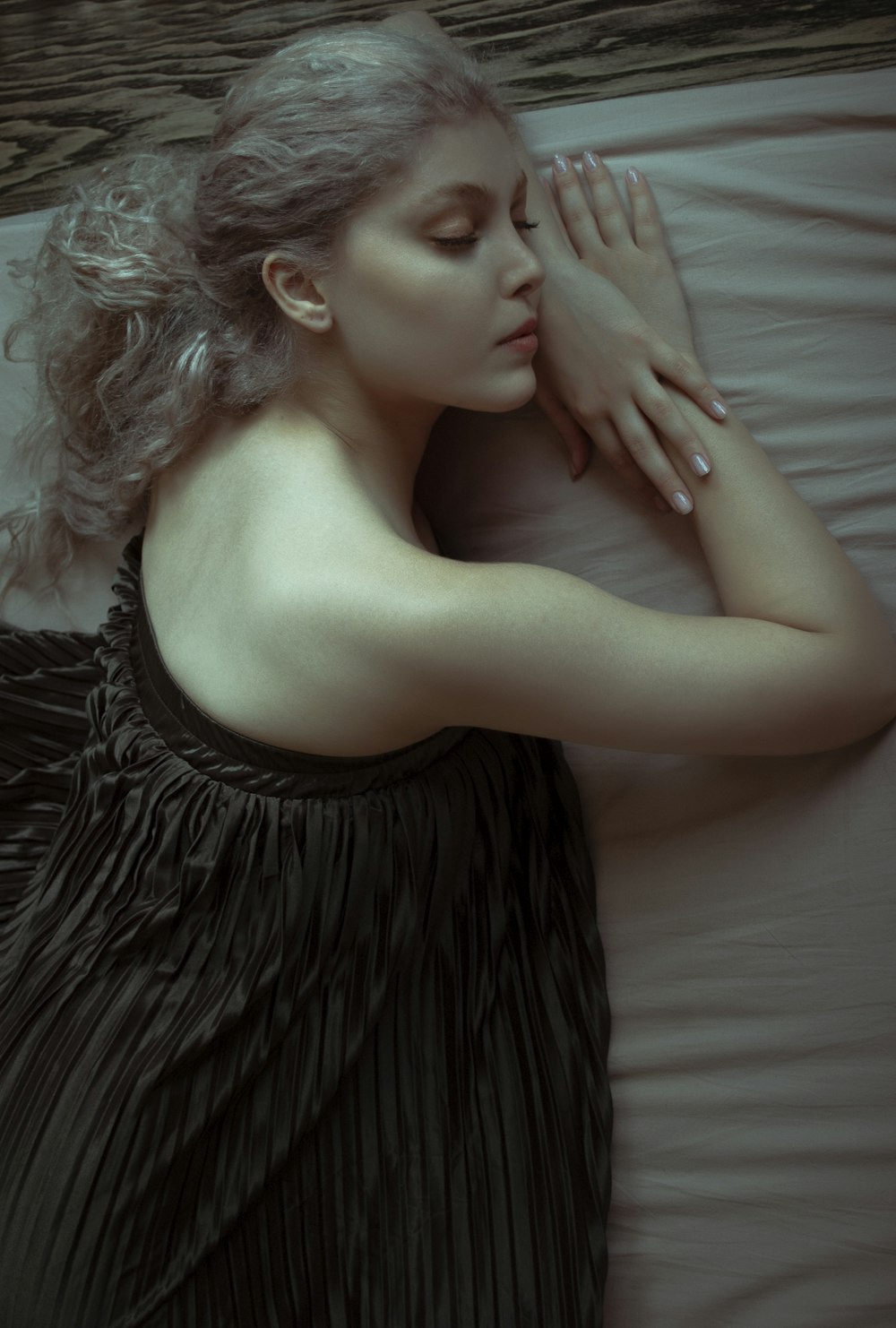 woman in black tube dress lying on white textile