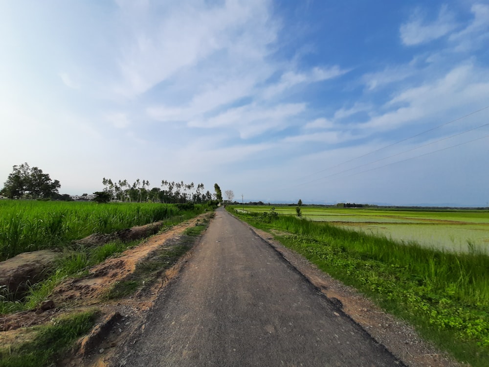 gray concrete road between green grass field under blue and white cloudy sky during daytime