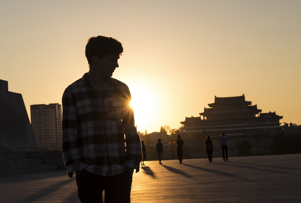 uomo in camicia a quadri bianca e nera in piedi sul pavimento di legno marrone durante il tramonto