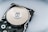 A close-up view of an opened hard disk drive, showcasing the shiny, reflective surface of the platter and the read/write head assembly. The metallic components are contrasted against a neutral background.