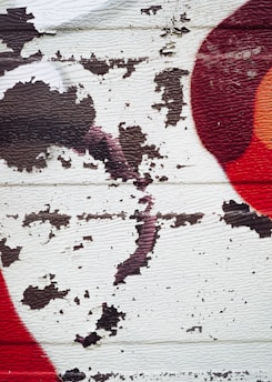 Peeling paint on a textured surface with abstract splashes of dark brown, red, and orange colors.