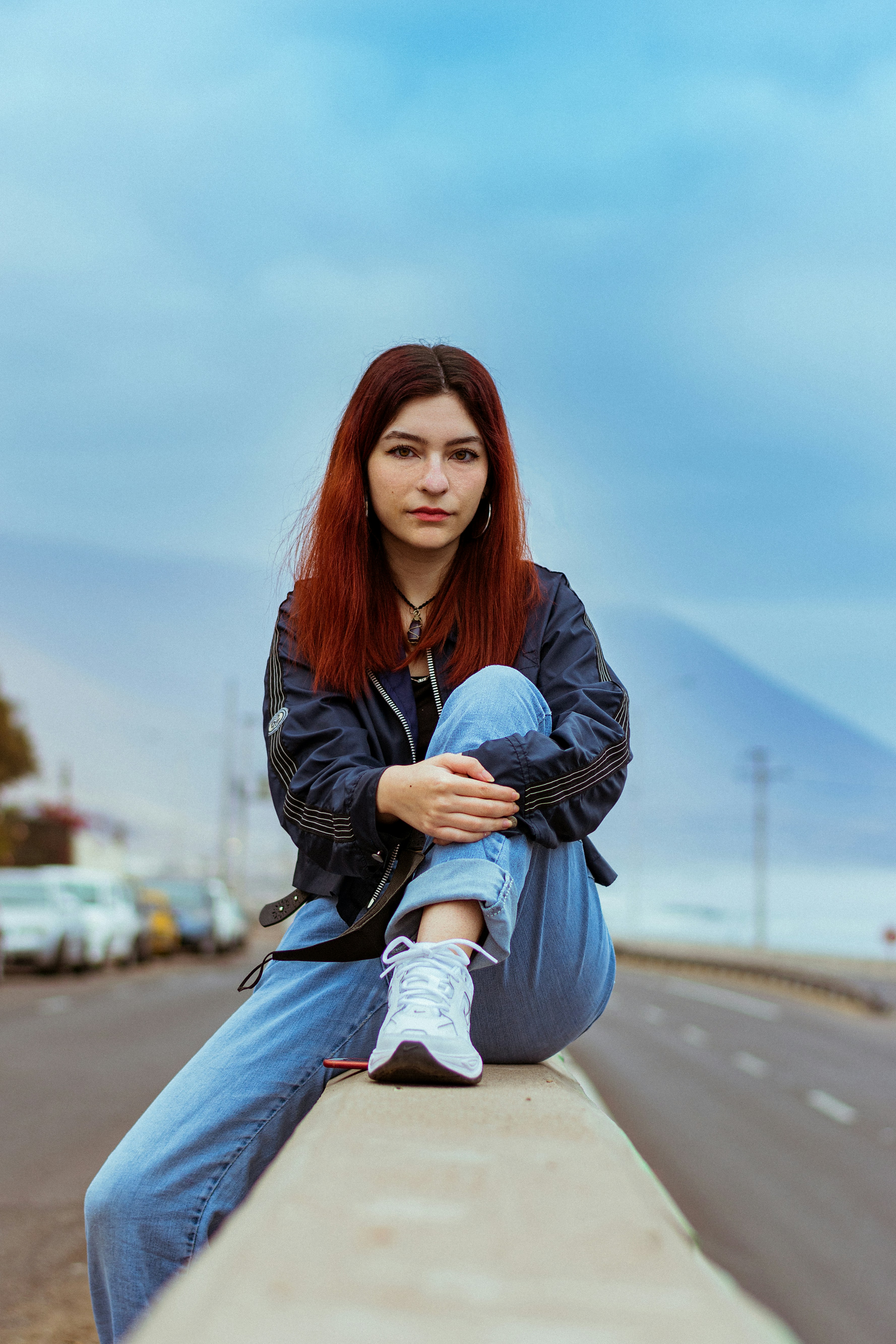 Woman in black jacket and blue denim jeans sitting on gray concrete ...