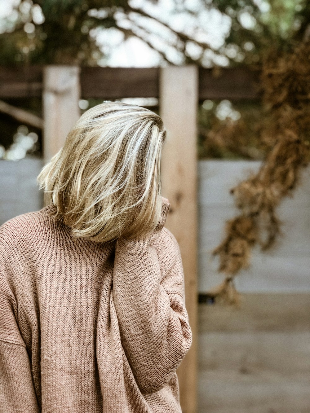 woman in brown sweater standing near brown wooden fence during daytime