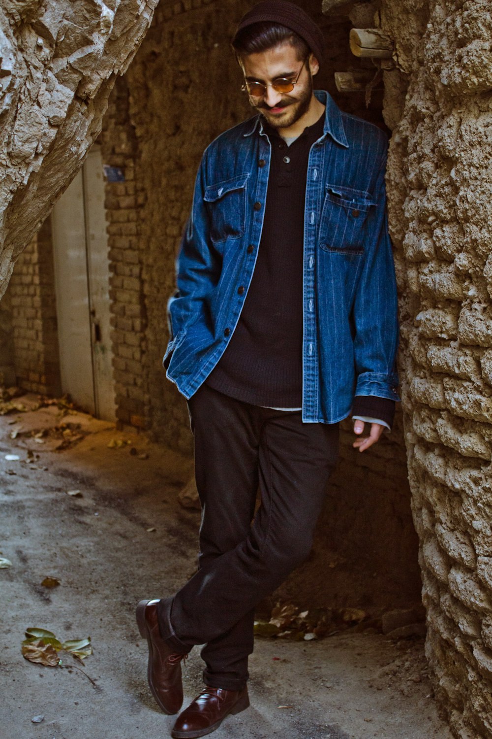 man in blue denim jacket standing beside brown brick wall