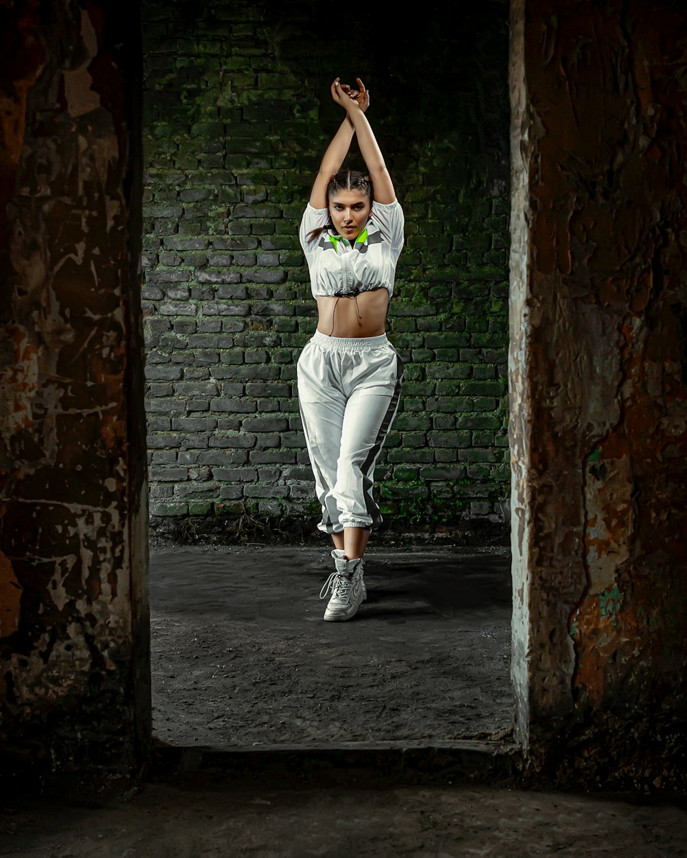 woman in white tank top and white pants standing in front of brown brick wall