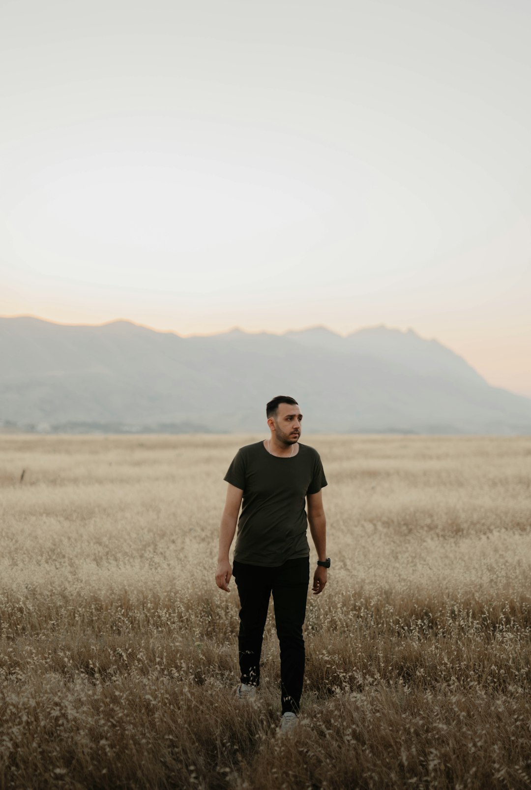 man in black crew neck t-shirt standing on brown grass field during daytime