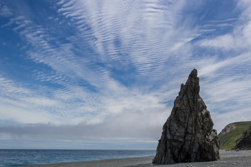 昼間の青空の下、海岸に浮かぶ灰色の岩層