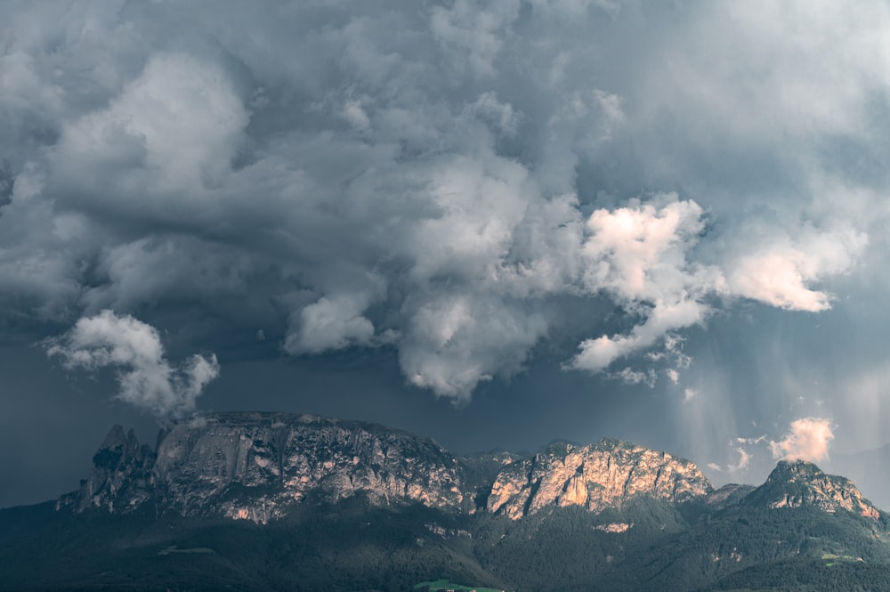 a mountain range under a cloudy sky with sunbeams